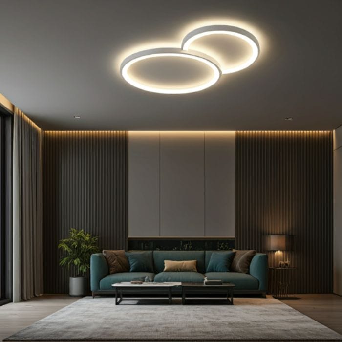 A modern living room with a double-ring ceiling light, featuring two concentric circles of light. The room has a gray wall, a teal sofa, a coffee table, and a plant. The overall atmosphere is clean and minimalist.