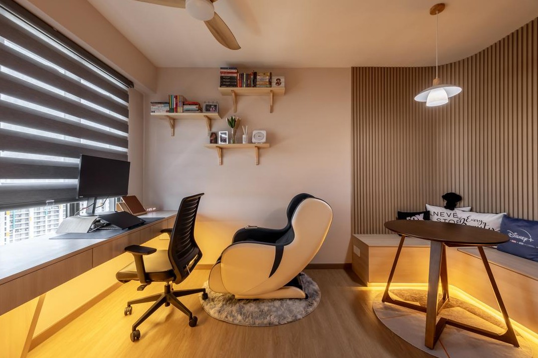 A cozy home office with a built-in desk and a comfortable massage chair. The room features warm lighting, wooden shelves, and a round table with a built-in bench.