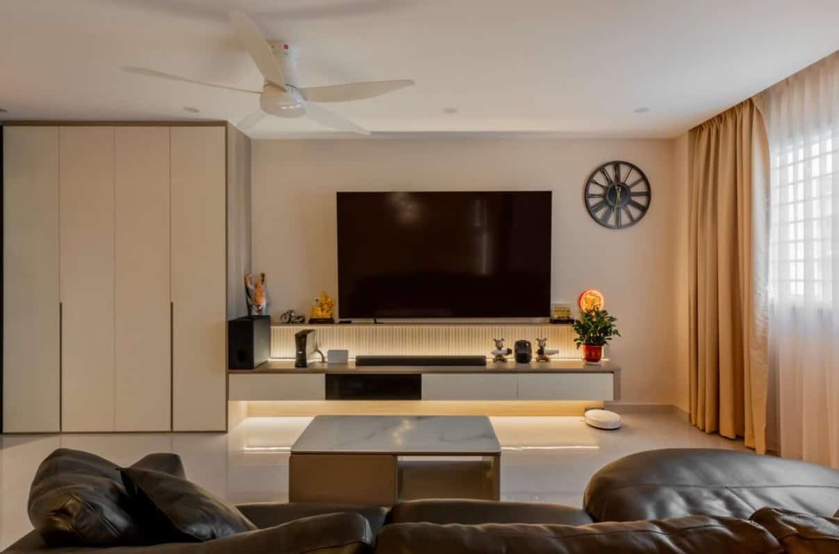 A cozy living room with a comfortable sofa, a flat-screen TV, and warm lighting. The room has a neutral color palette and features a ceiling fan for added comfort.