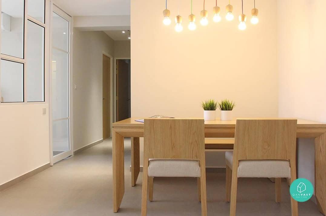 A minimalist dining area with a wooden dining table and chairs. The room is lit by a row of pendant lights hanging over the table, creating a warm and inviting atmosphere.