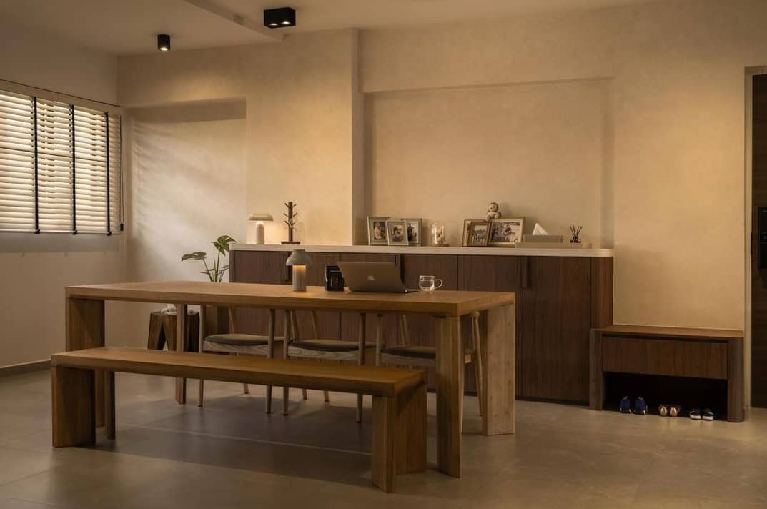 A minimalist living room with a long, wooden dining table and bench. The room features warm, neutral tones and soft lighting, creating a cozy and inviting atmosphere.