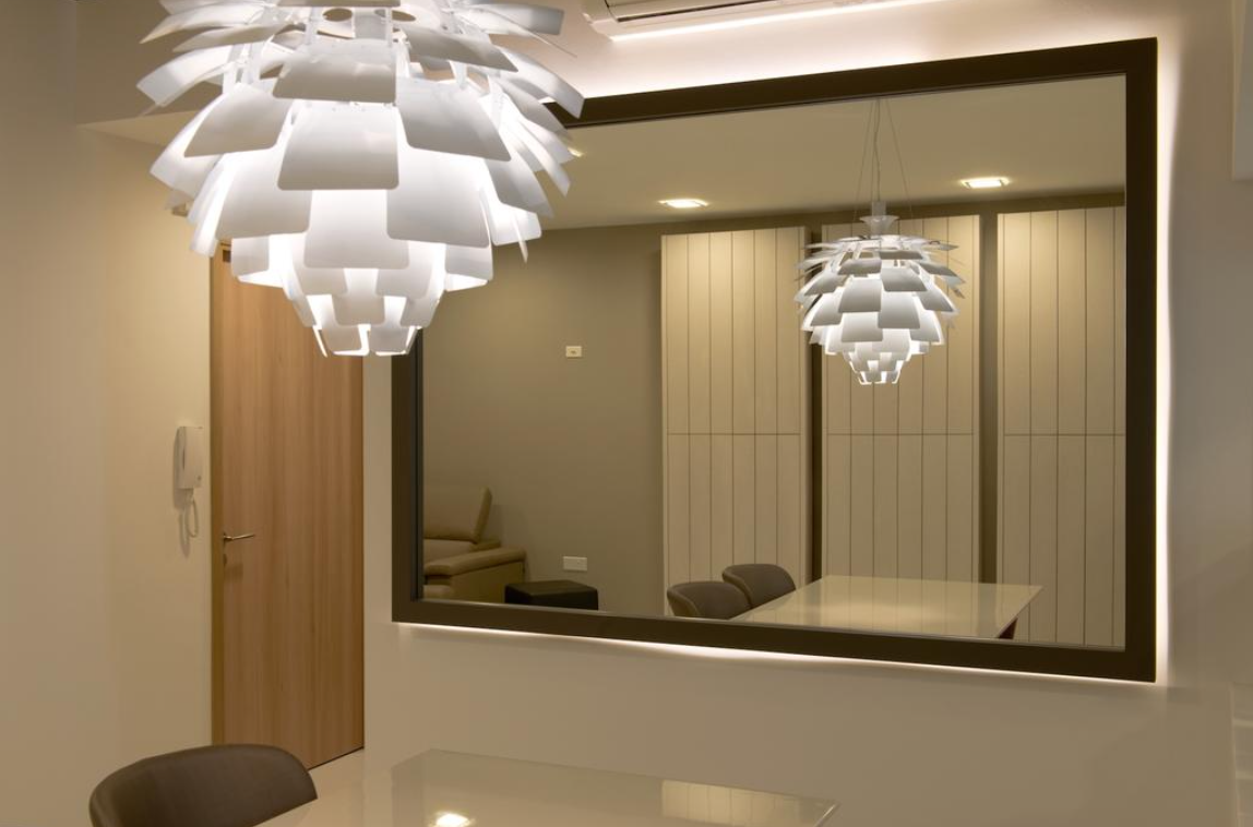 A modern dining room with a large mirror reflecting the space, creating an illusion of depth. Two unique, sculptural pendant lights hang above the dining table, adding a touch of artistic flair to the room.