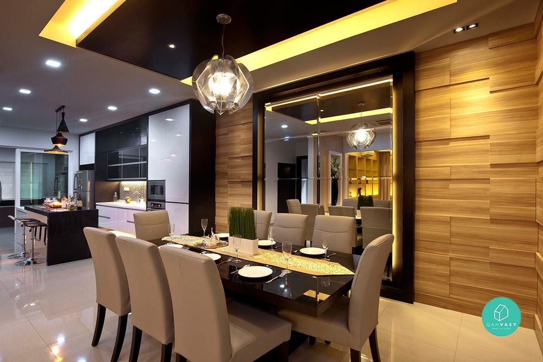 A modern dining room with a large rectangular dining table and chairs. The room features a dramatic ceiling with recessed lighting and a unique geometric chandelier. A mirrored wall creates a sense of spaciousness and reflects the light.