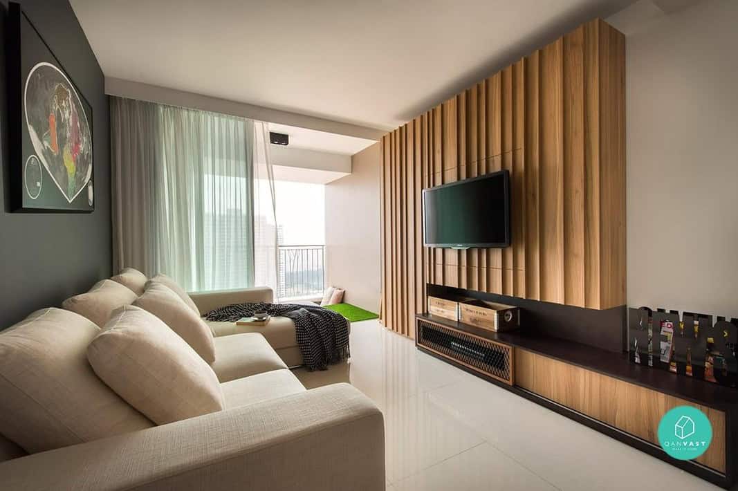 A modern living room with a sleek, wood-paneled wall that houses a flat-screen TV. The room features a comfortable sofa, a coffee table, and large windows that let in plenty of natural light.