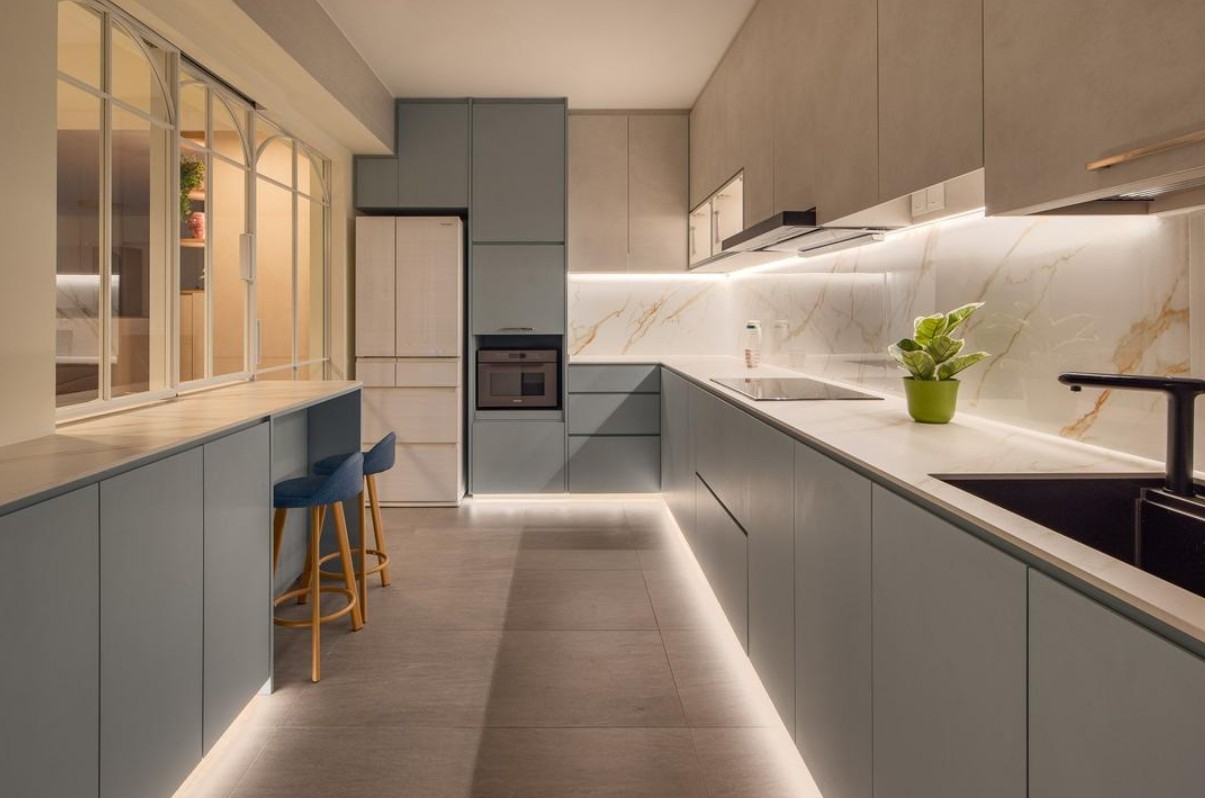 A modern, minimalist kitchen with sleek blue cabinetry and a white marble countertop. The kitchen features integrated LED lighting under the upper cabinets, providing ample task lighting for food preparation. The overall aesthetic is clean, contemporary, and functional.