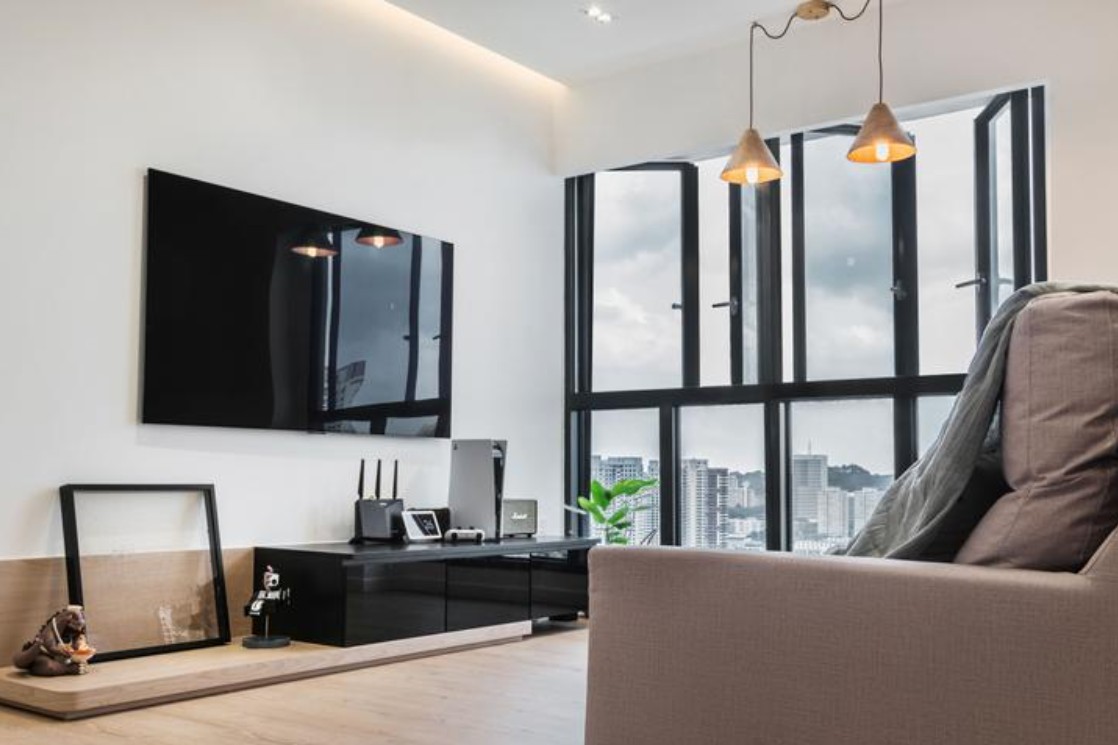 A modern living room with a large TV mounted on the wall, a comfortable sofa, and a coffee table. The room features a minimalist design with clean lines and neutral colors. The lighting is minimal, with a few sleek pendant lights hanging above the coffee table.