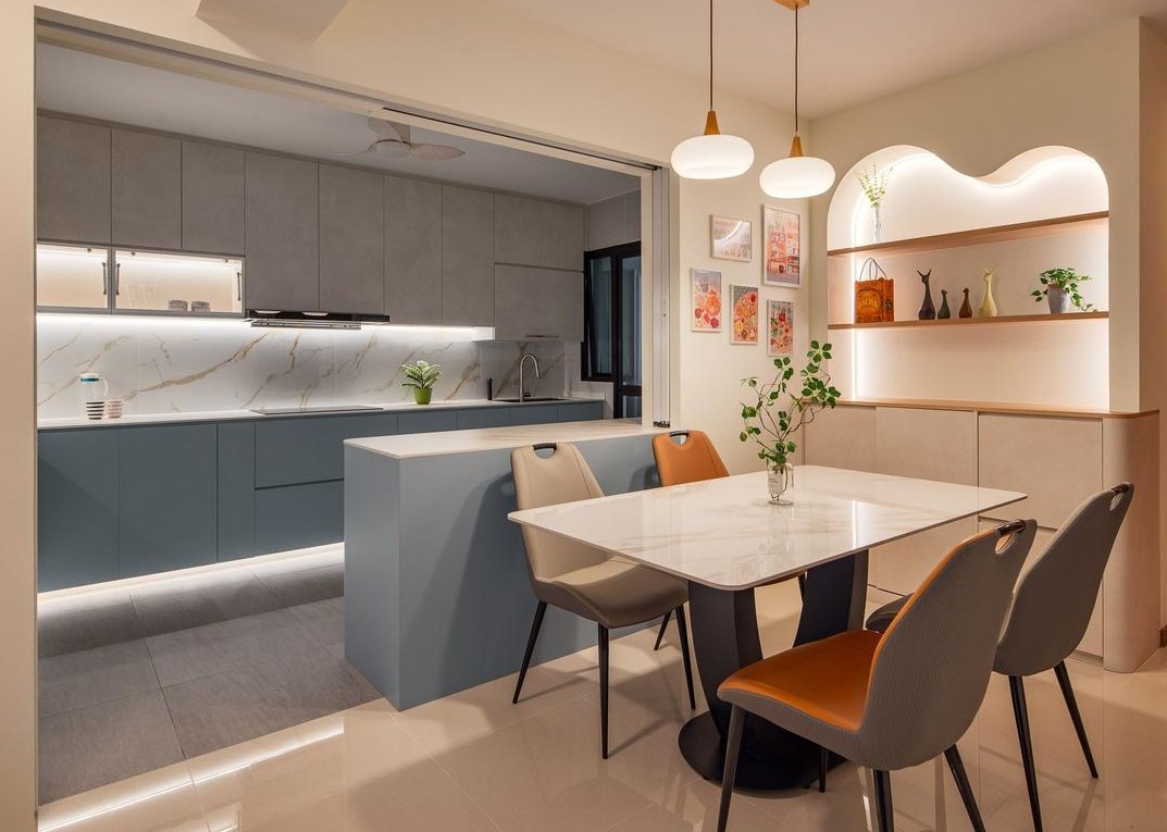 A modern, open-concept kitchen and dining area with a minimalist design. The kitchen features a white marble countertop, blue cabinetry, and under-cabinet lighting. The dining area has a round table with white marble top, and stylish chairs. The overall aesthetic is clean, contemporary, and inviting.