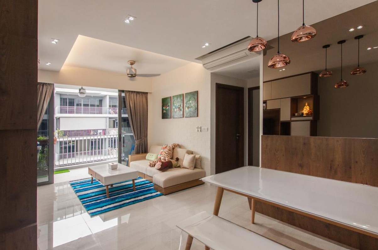 A modern open-concept living space with a beige sofa, colorful throw pillows, and a blue rug. The dining area features a white table and chairs. The ceiling features recessed lighting and a ceiling fan, while a row of pendant lights adds a stylish touch.