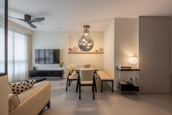 A modern open-concept living and dining area with a beige color scheme. The space features a comfortable sofa, a dining table with chairs, and a built-in shelf with decorative items. The ceiling features a stylish chandelier and a ceiling fan, providing both ambiance and functionality.